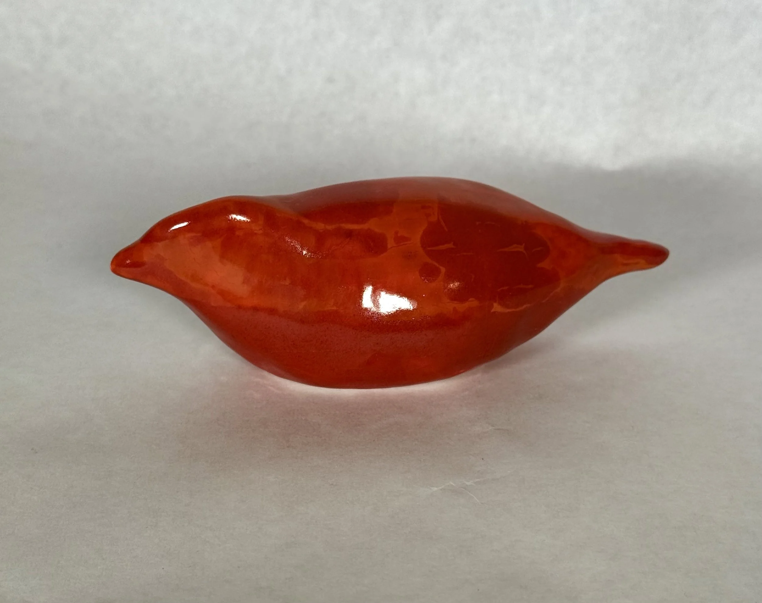 Close-up of a shiny red object resembling a chili pepper on a light gray surface.