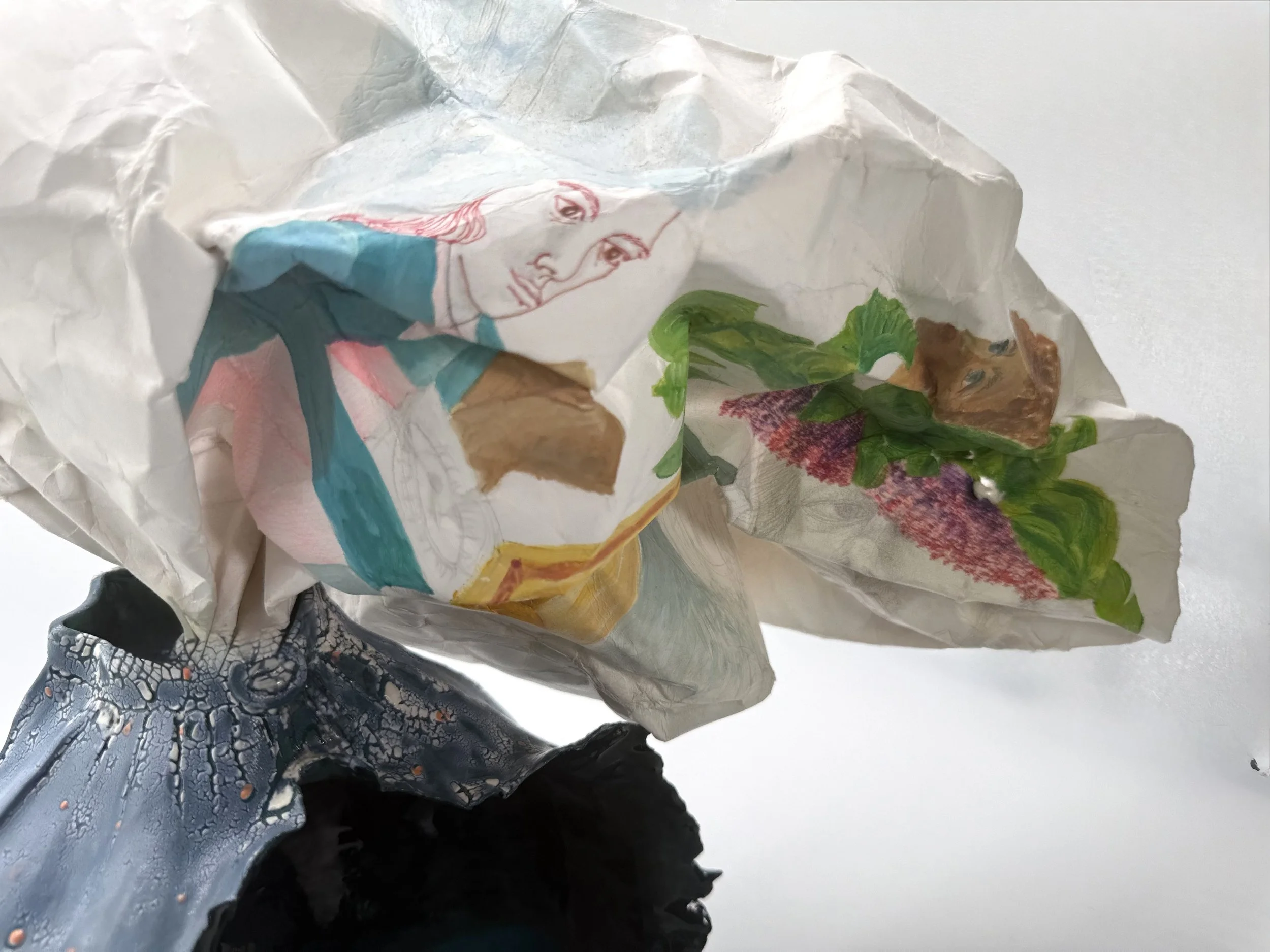 Crumpled paper with printed and drawn images, including a woman’s face, green leaves, and other colorful illustrations.