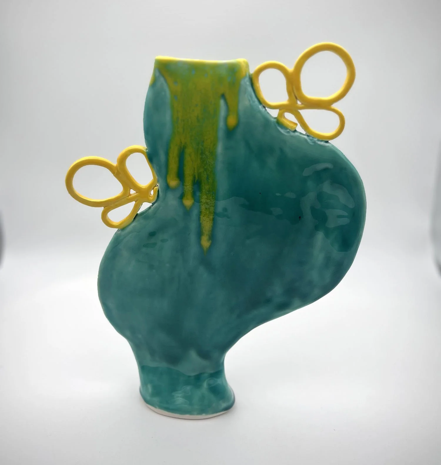 A ceramic art piece resembling a human heart with vibrant turquoise glaze, and yellow pair of wire connected grandfather style glasses perched on top.