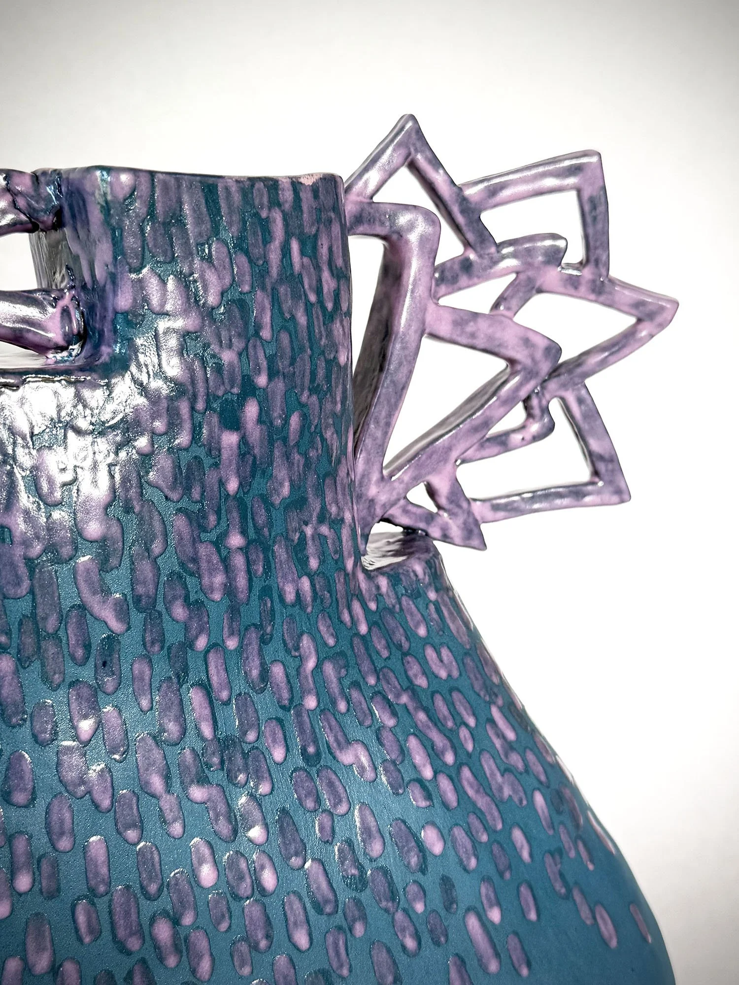 Close-up of a colorful, textured ceramic object with purple, blue, and pink hues, featuring geometric cutouts at the top.