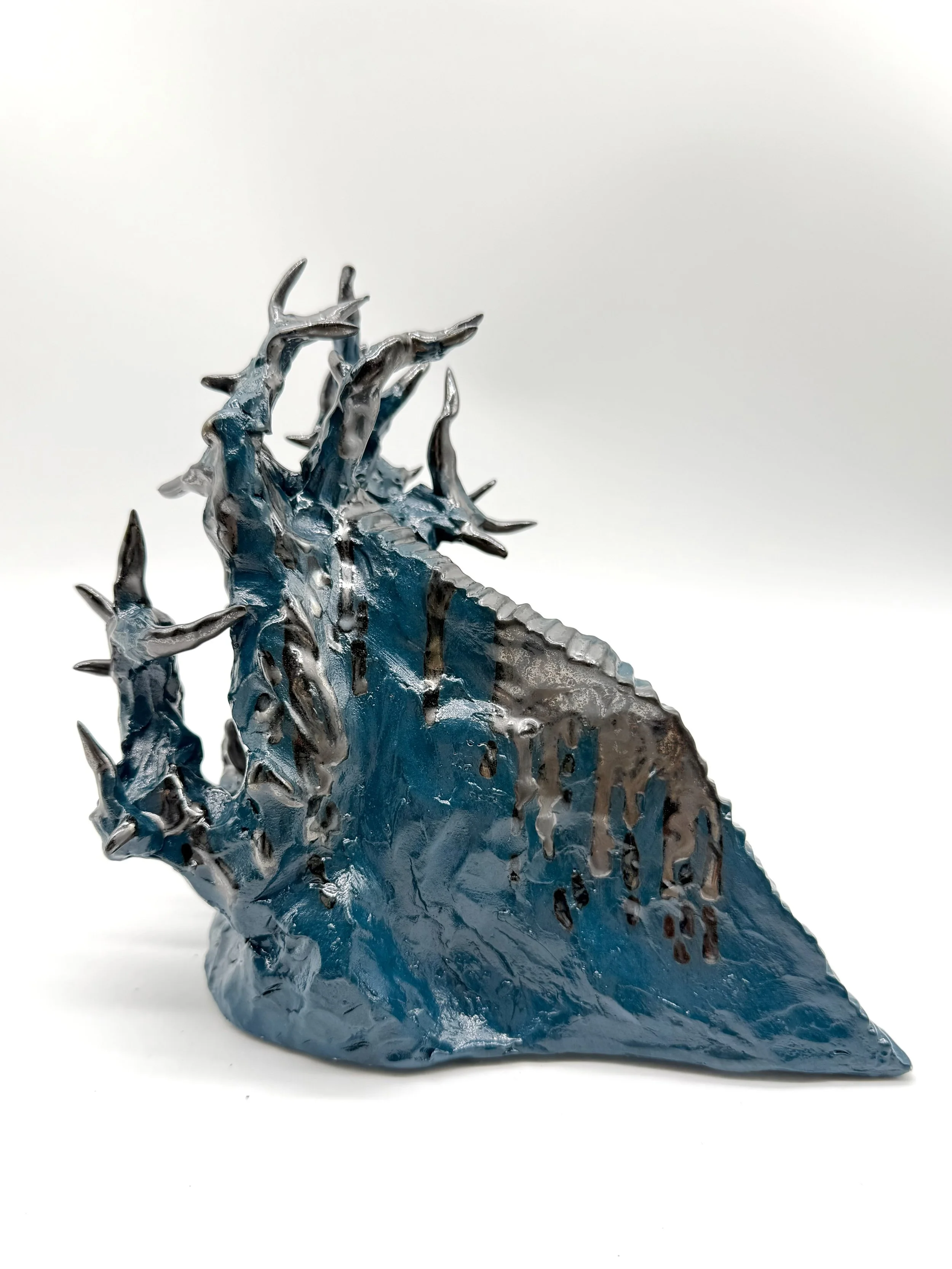 A glass sculpture of a blue dragon with silver accents and sharp, spiky features on its head, back, and tail, set against a white background.