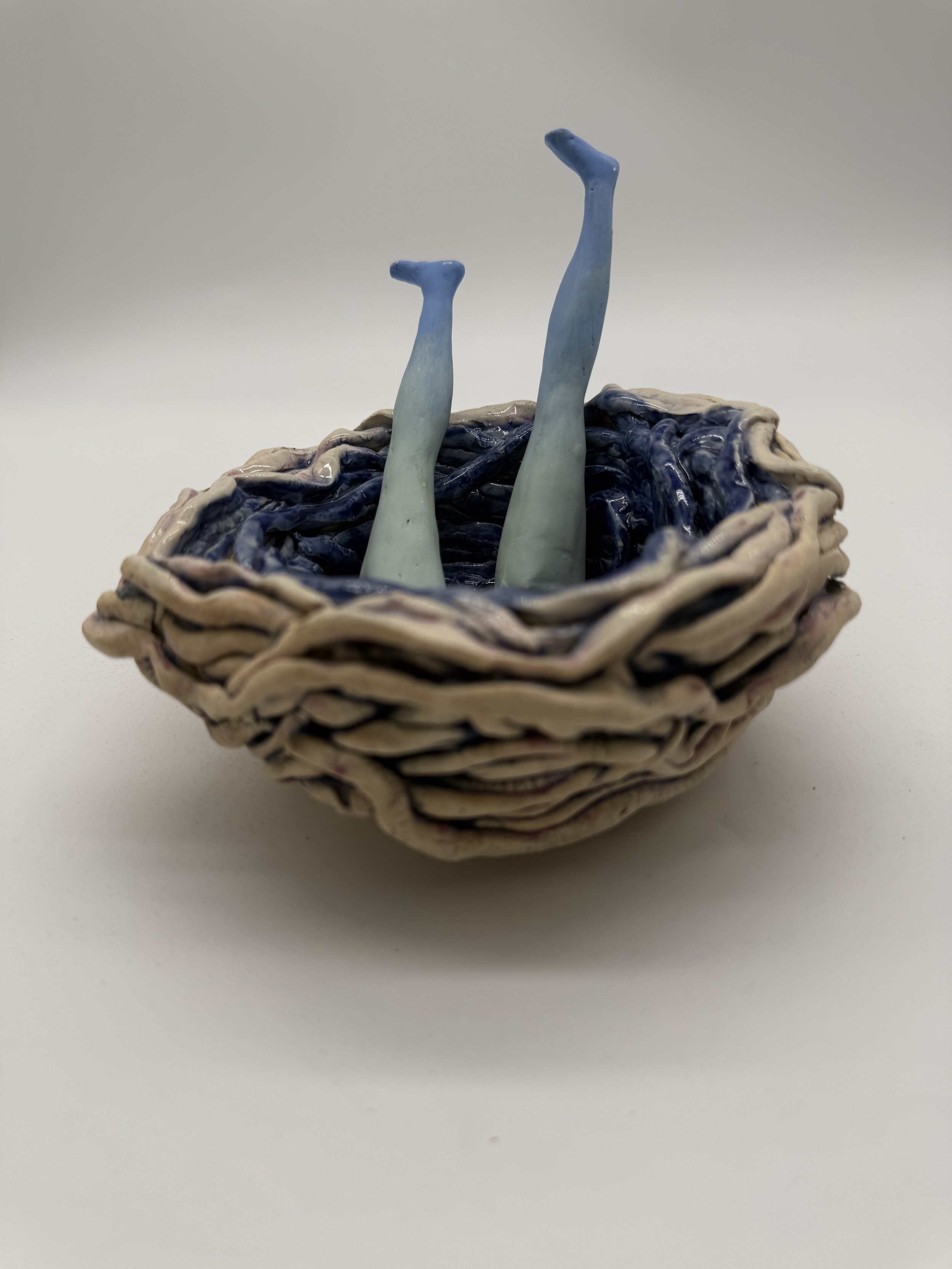 A ceramic basket with two ceramic legs sticking out, decorated in blue and white glaze.
