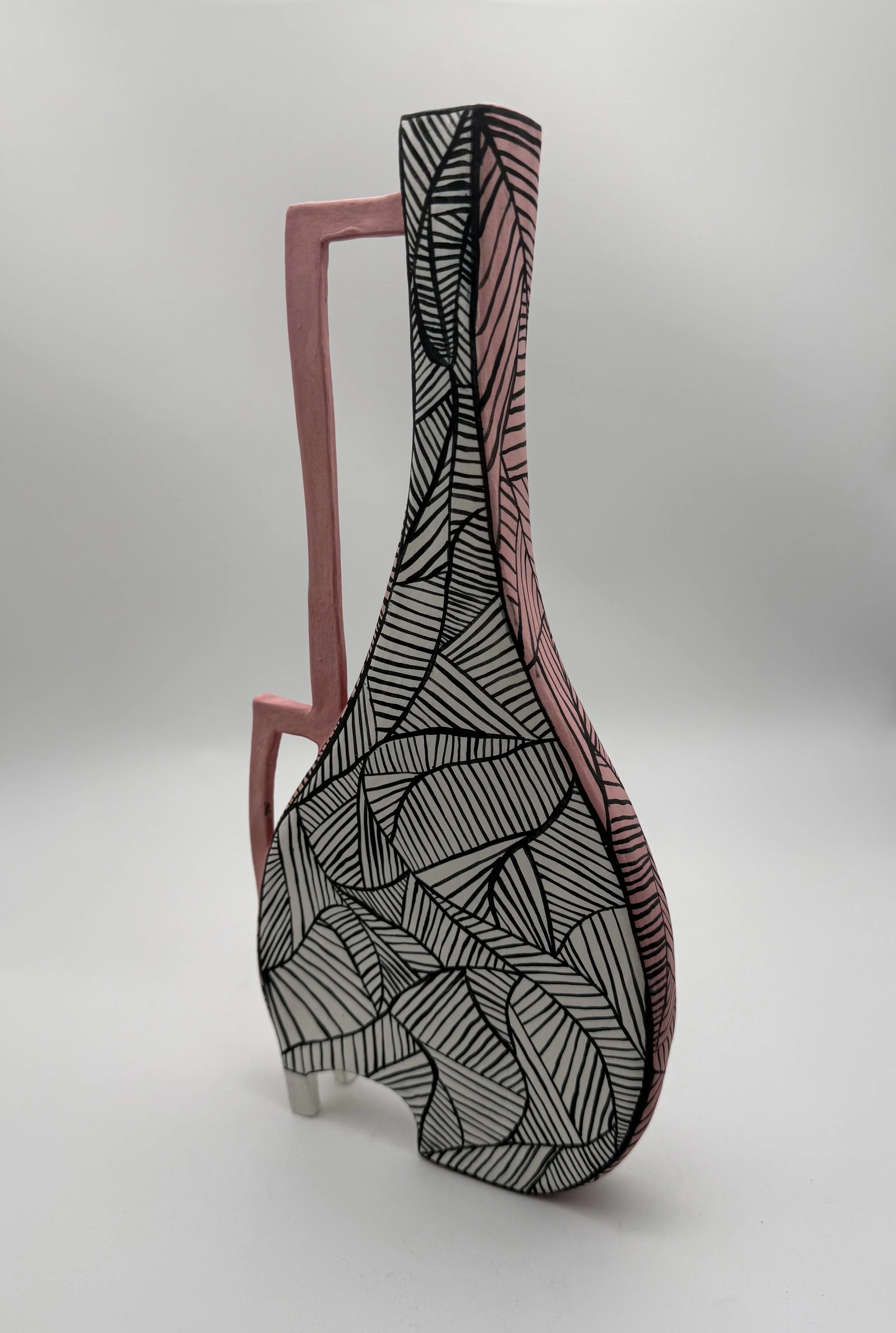 Decorative standing sculpture resembling a high-heeled shoe, with black and white leaf pattern on the shoe part, and pink structure resembling a shoehorn or frame on a white background.