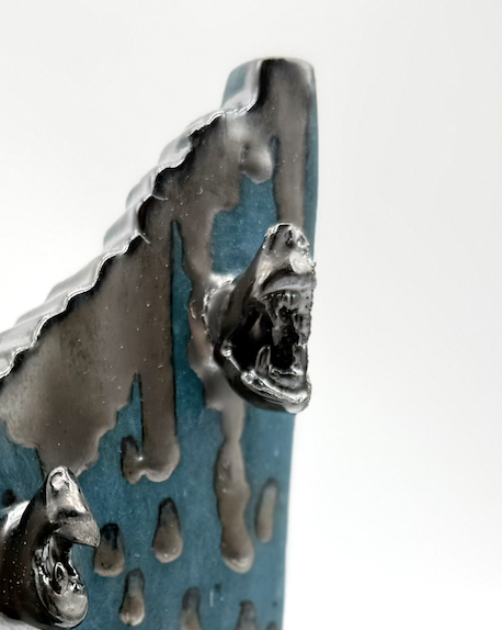 Close-up of a metallic object with a shark head design, featuring sharp teeth and textured surface.