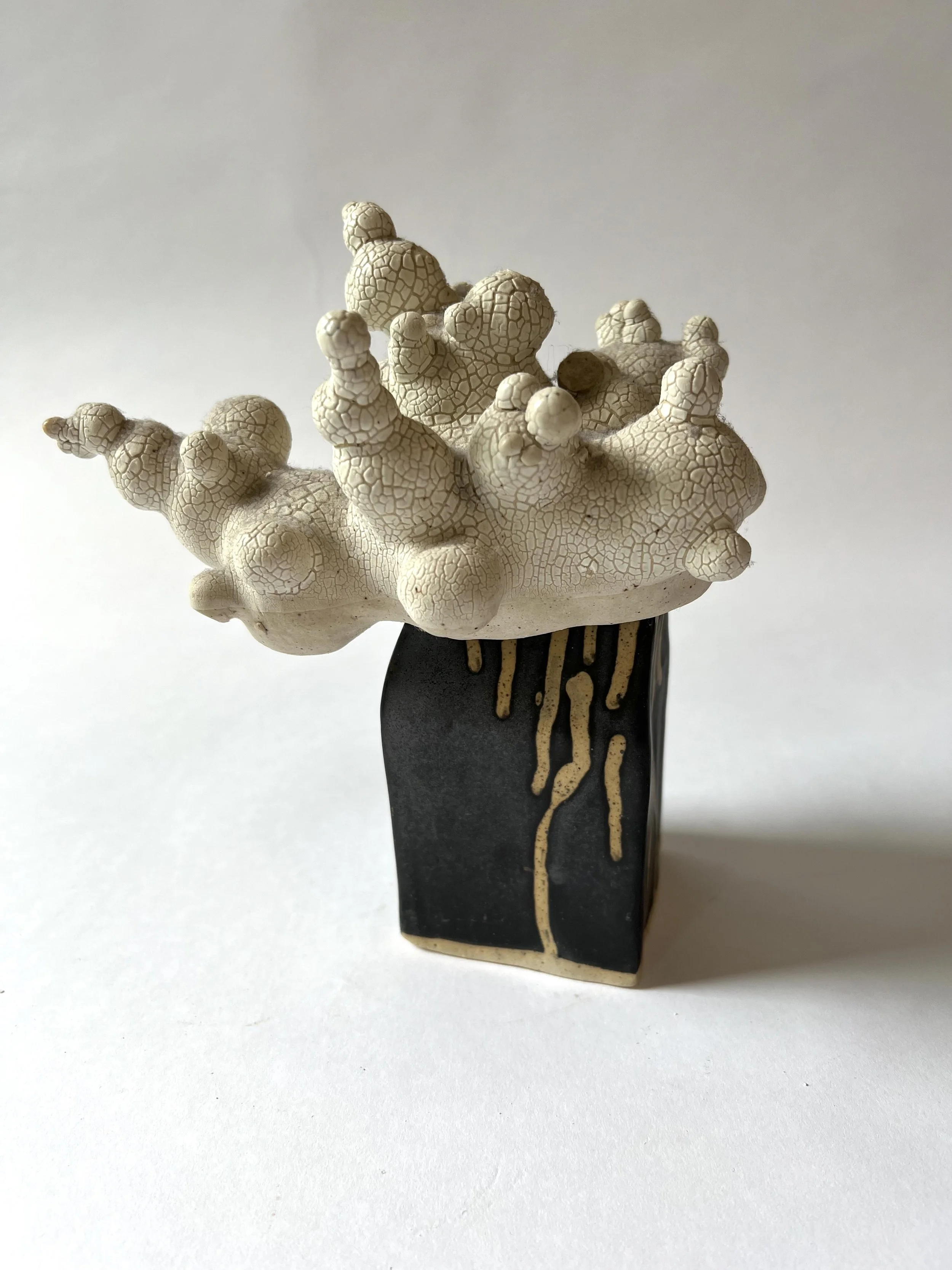 A ceramic sculpture resembling a cloud with multiple rounded protrusions, mounted on a black base with a gold drip design.