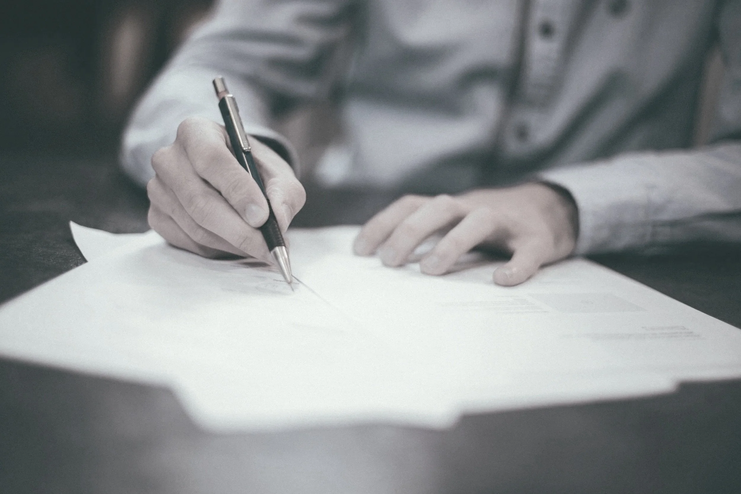 A person writing with a silver pen on white paper.