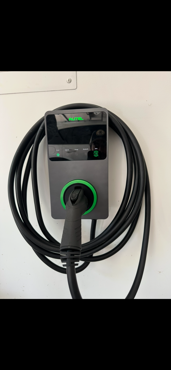 Electric vehicle charging station with a black power cable coiled around it and a display screen showing the brand 'Autel'.