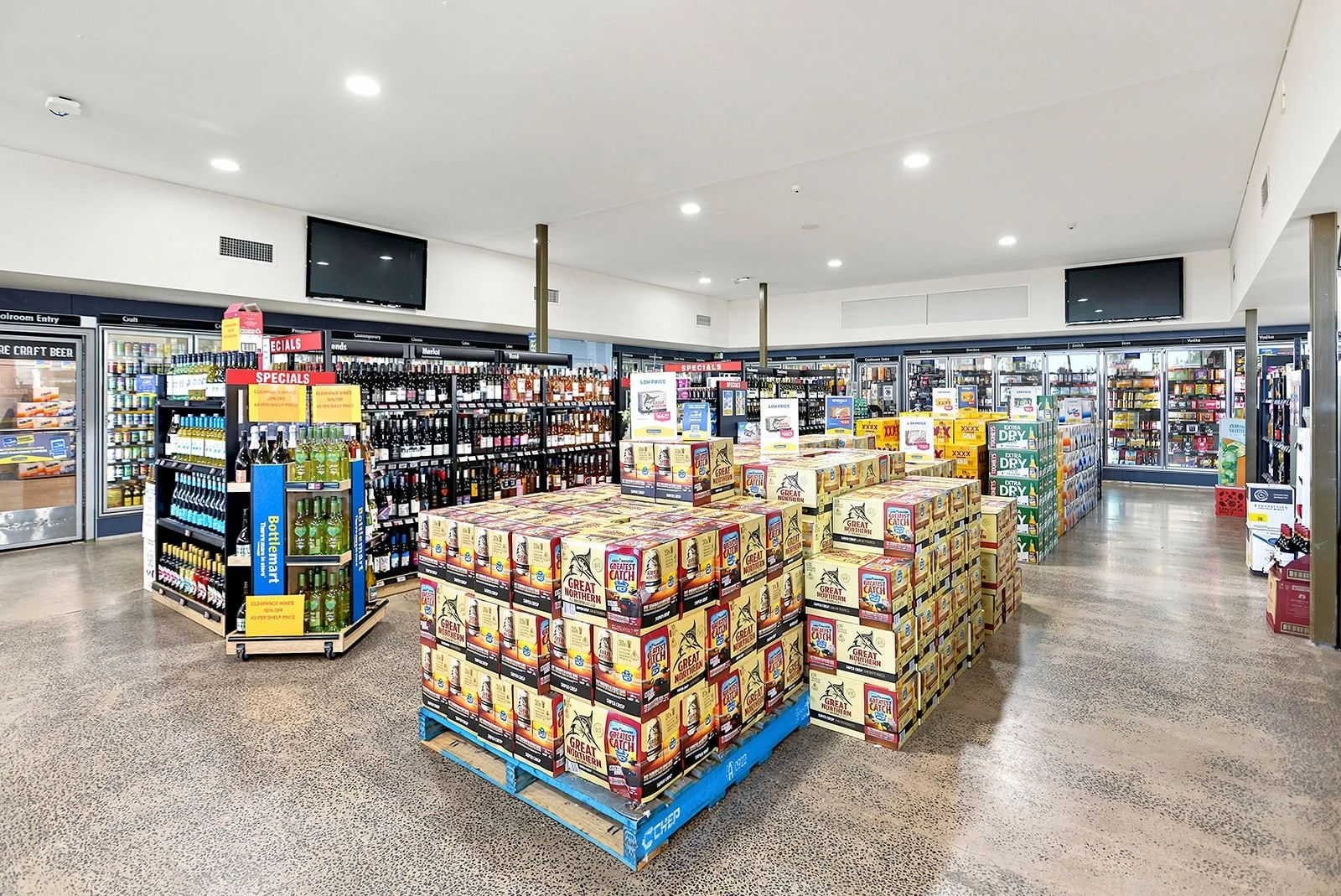 Interior of a grocery store with shelves and displays of beverages, snacks, and alcohol. The floor is polished and the ceiling has bright recessed lighting.