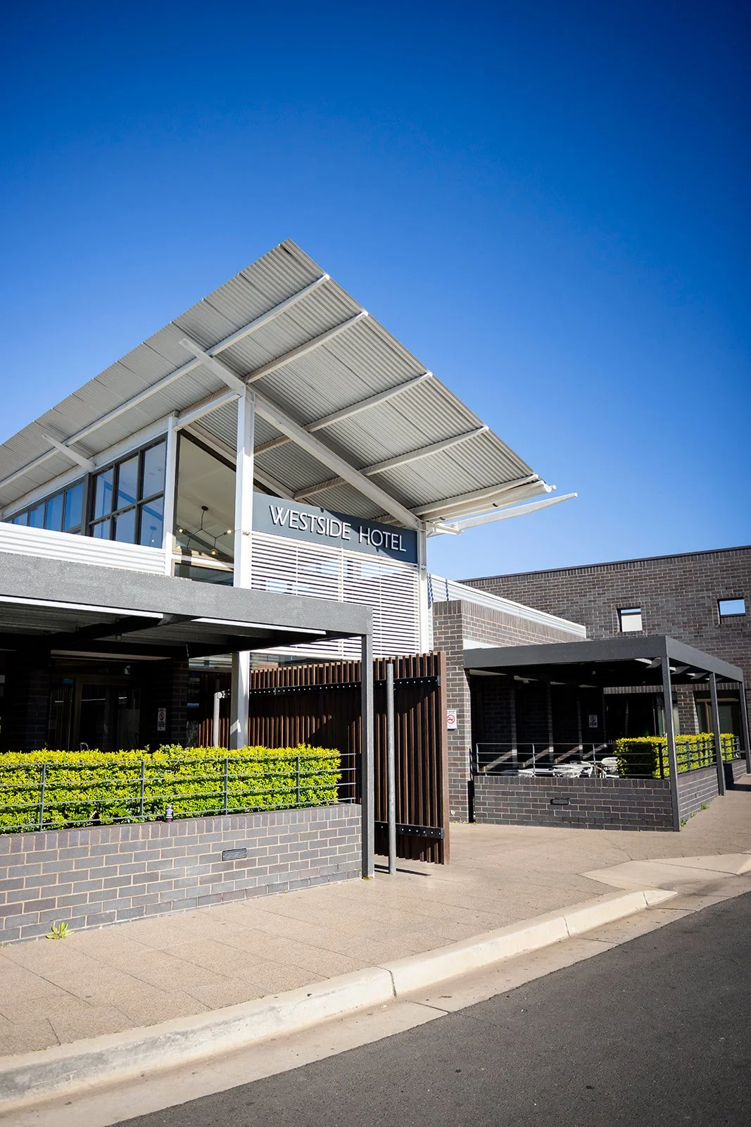 Exterior of Westside Hotel with modern architecture, metal roof, glass windows, and a clear blue sky.