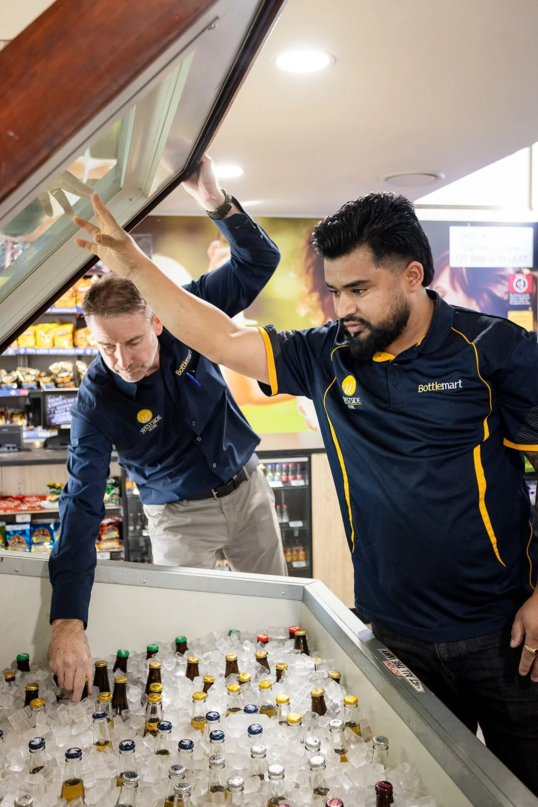 Two employees stocking bottled beverages in a freezer at a convenience store.