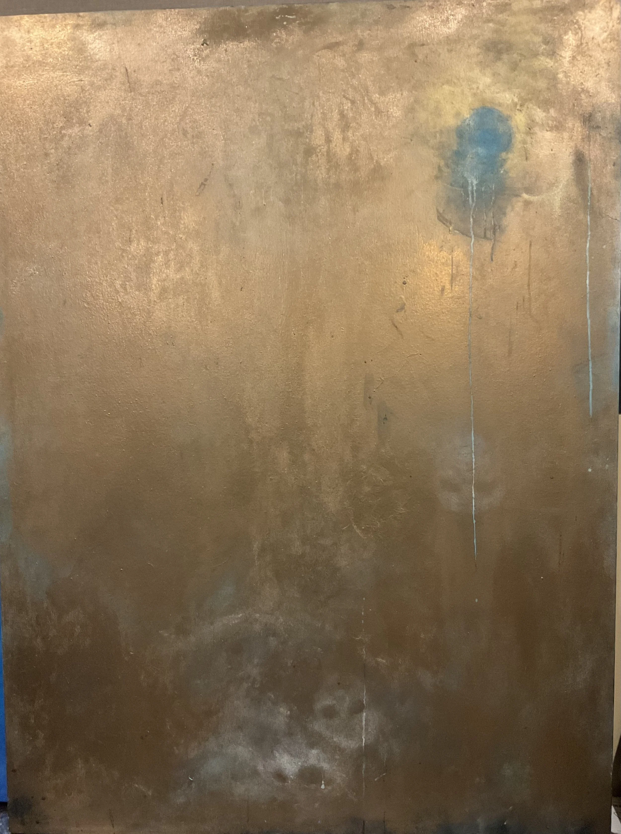 A worn, gold-colored metal surface with a small blue object or stain toward the upper right side and a vertical line running down the right side.