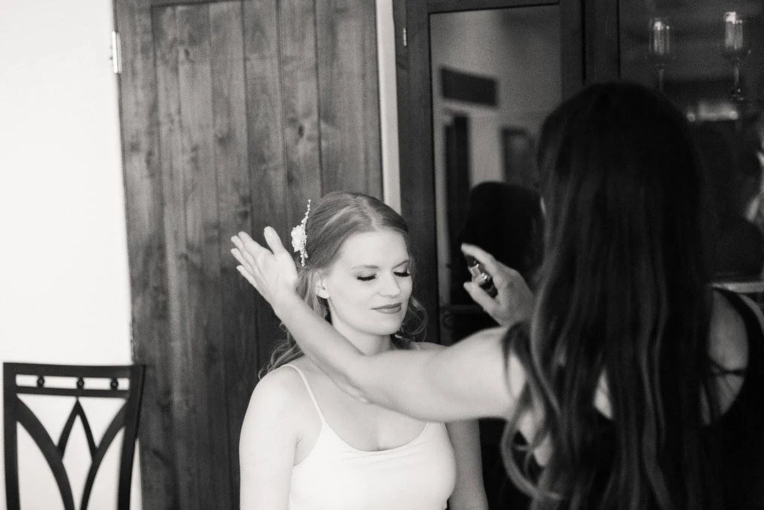 Woman with closed eyes having makeup applied by a makeup artist in a room with wooden wall