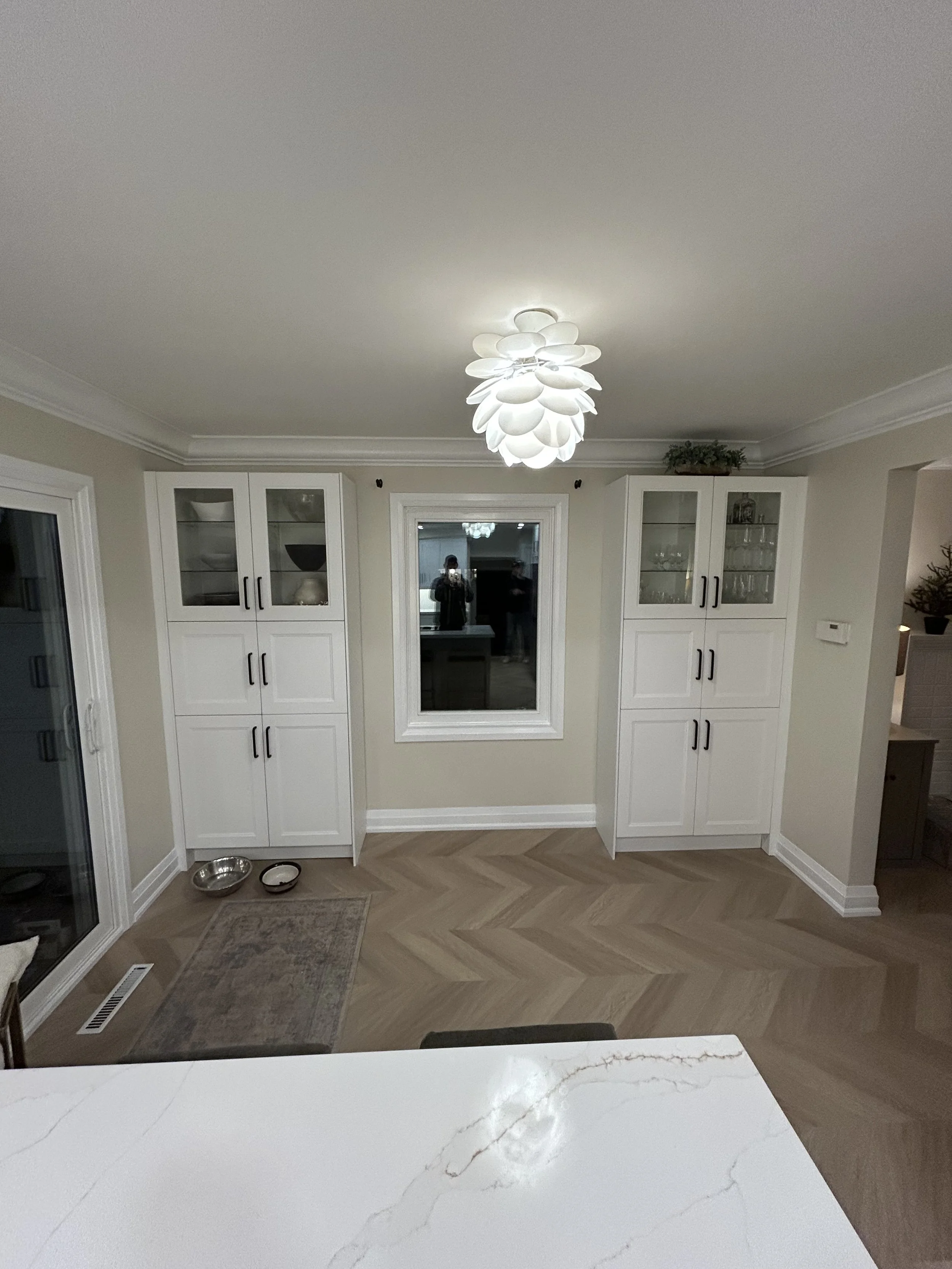 A kitchen interior with white cabinets, a large window, and a white marble countertop with brown veining.