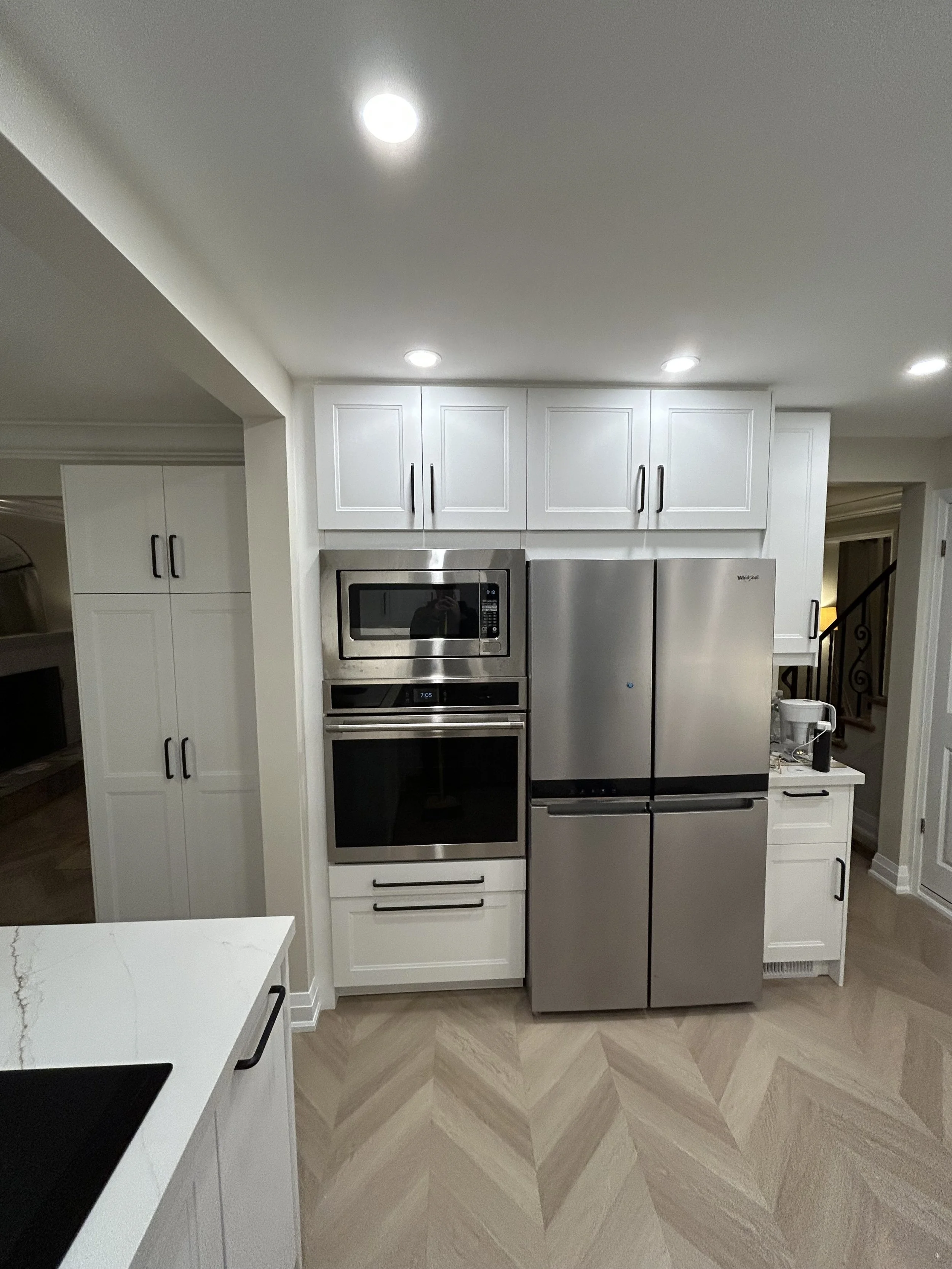 Modern kitchen with white cabinetry, built-in microwave, stainless steel refrigerator, and granite countertops, with beige tile flooring.