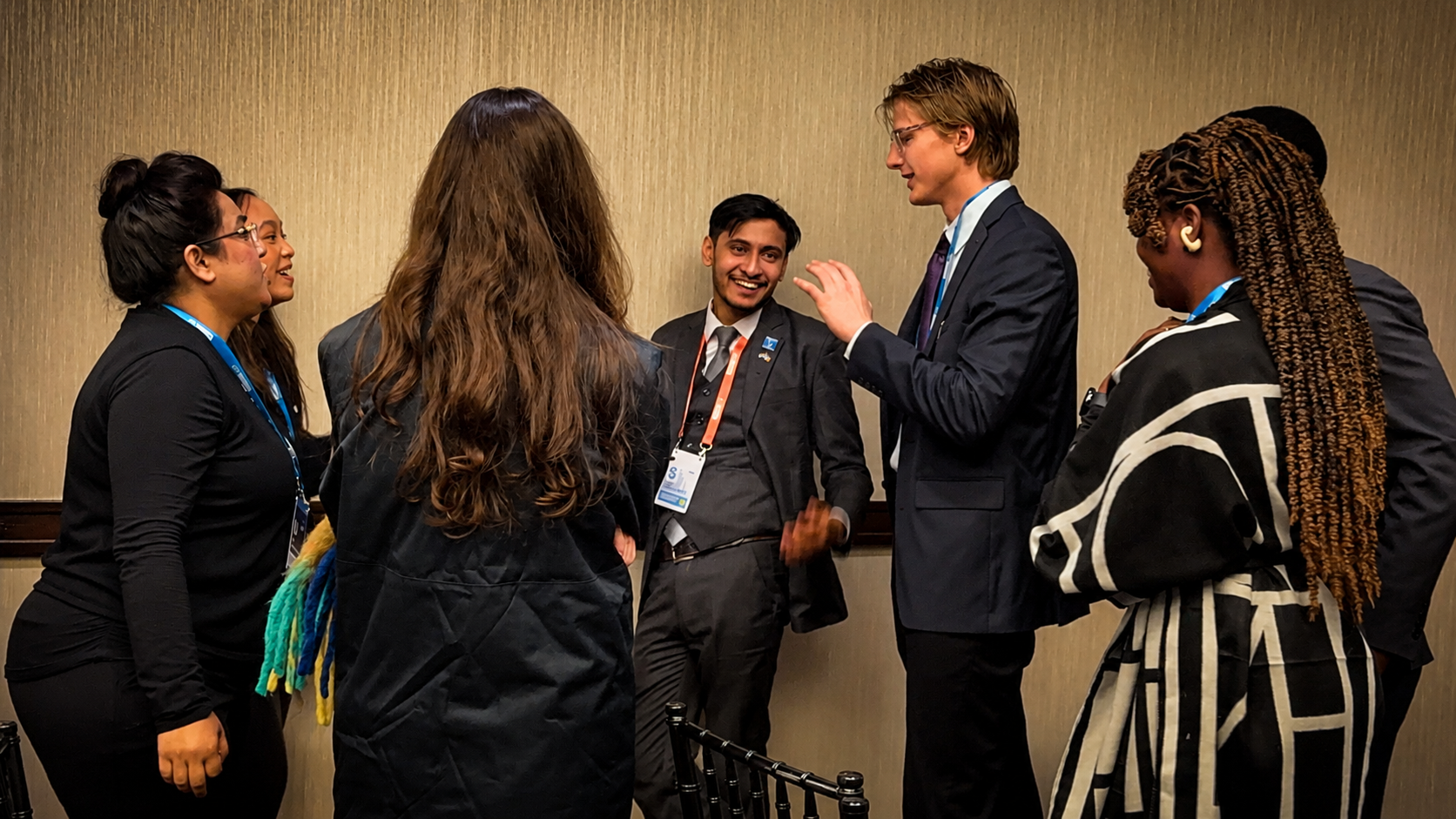 Group of diverse people in professional attire engaged in conversation in a conference room, some smiling and gesturing.