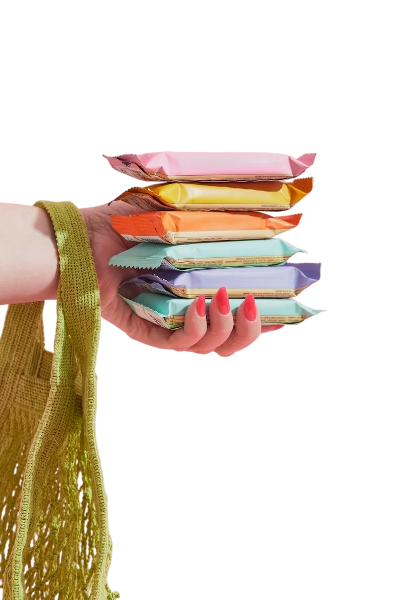 Hand holding a stack of various colorful packaged wet wipes, with a yellow cloth draped over the wrist.