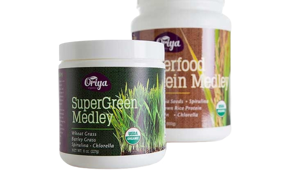 Two containers of Oriya Super Green Medley with ingredients listed as wheat grass, barley grass, spirulina, and chlorella. One container is in front, and the other is in the background.