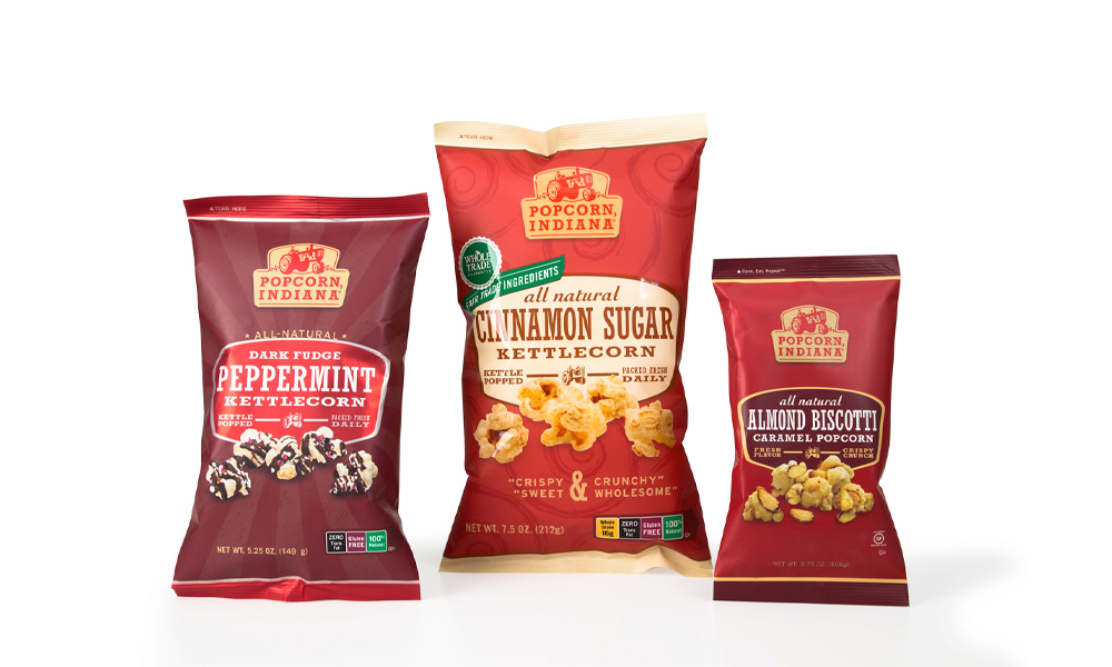 Three bags of Popcorn Indiana popcorn flavors: dark fudge peppermint kettlecorn, cinnamon sugar kettlecorn, and almond biscoff caramel popcorn.