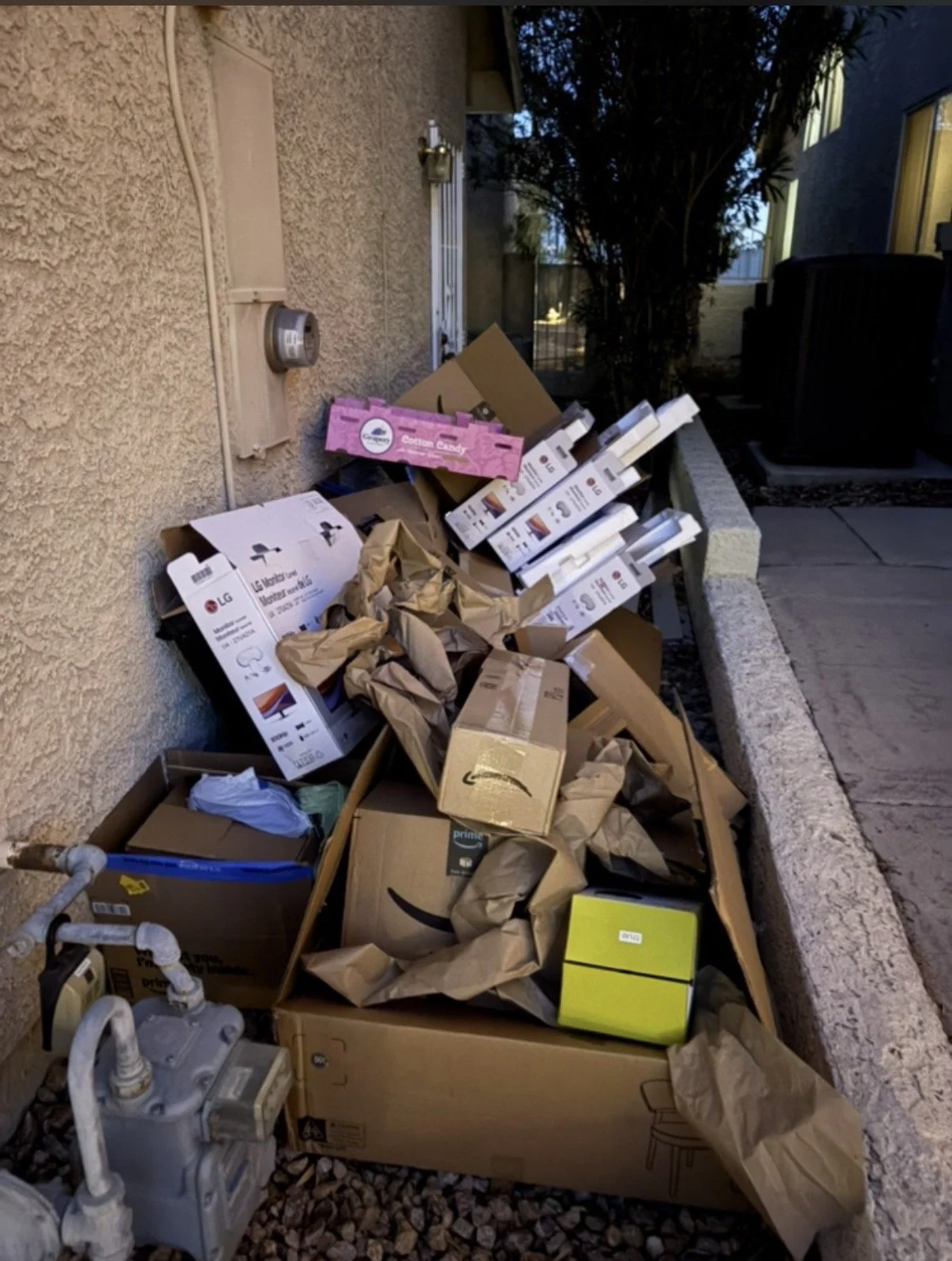 Overflow of paper shopping bags, cardboard boxes, and packaging materials outside a building near a wall.
