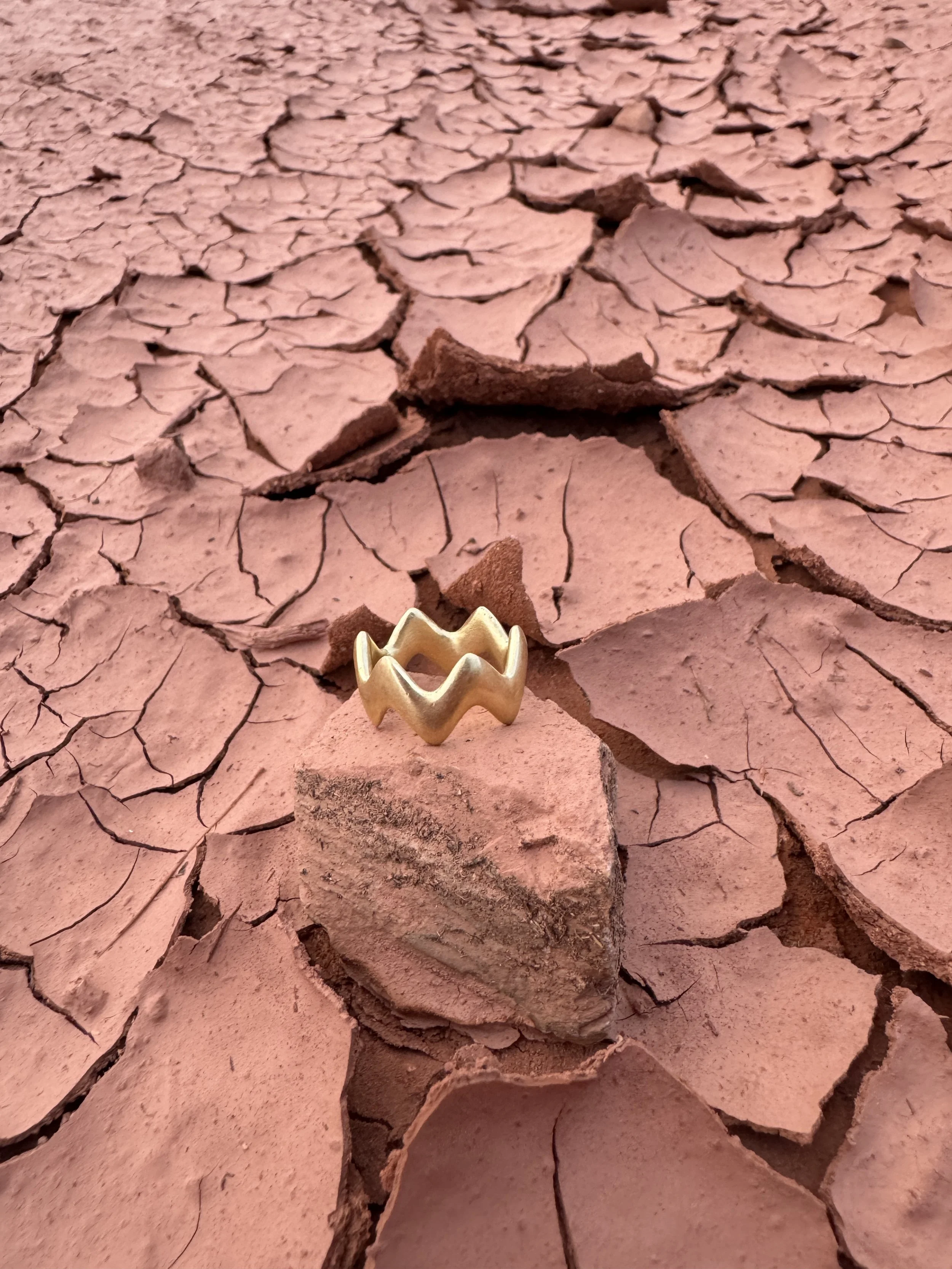 GemLost Desert ZigZag Ring in solid 18k gold resting on cracked red desert earth.
