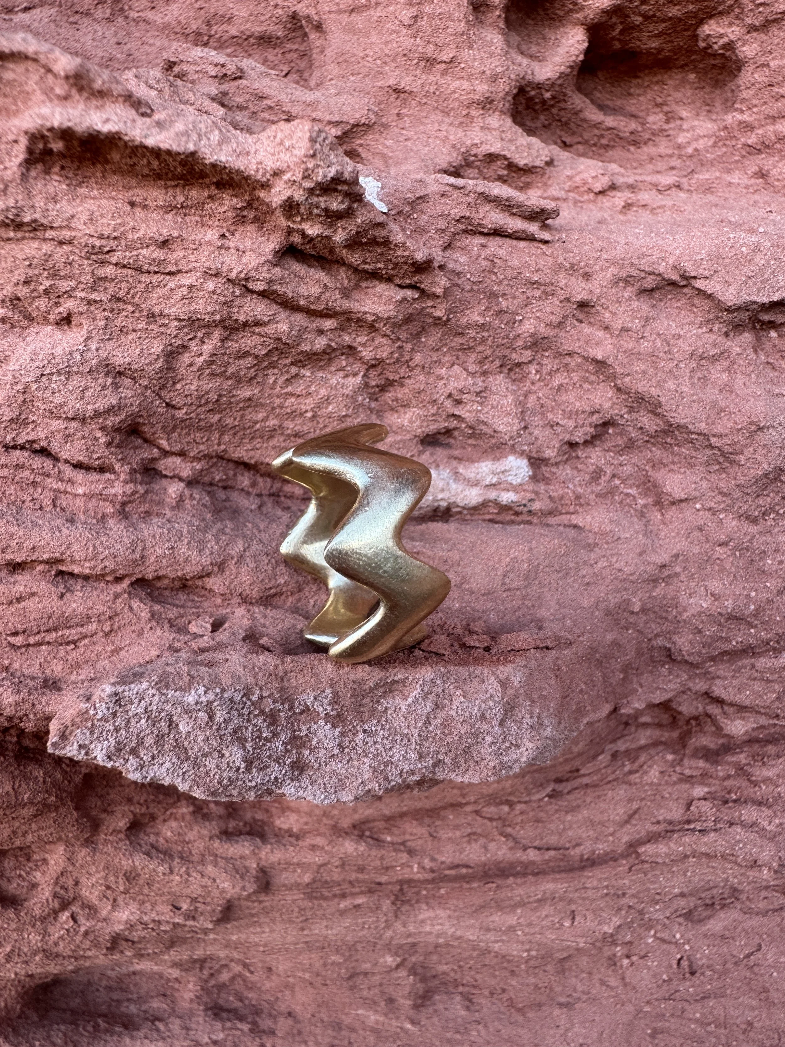 GemLost Desert ZigZag Ring in solid 18k gold shown in side profile resting on layered red rock.