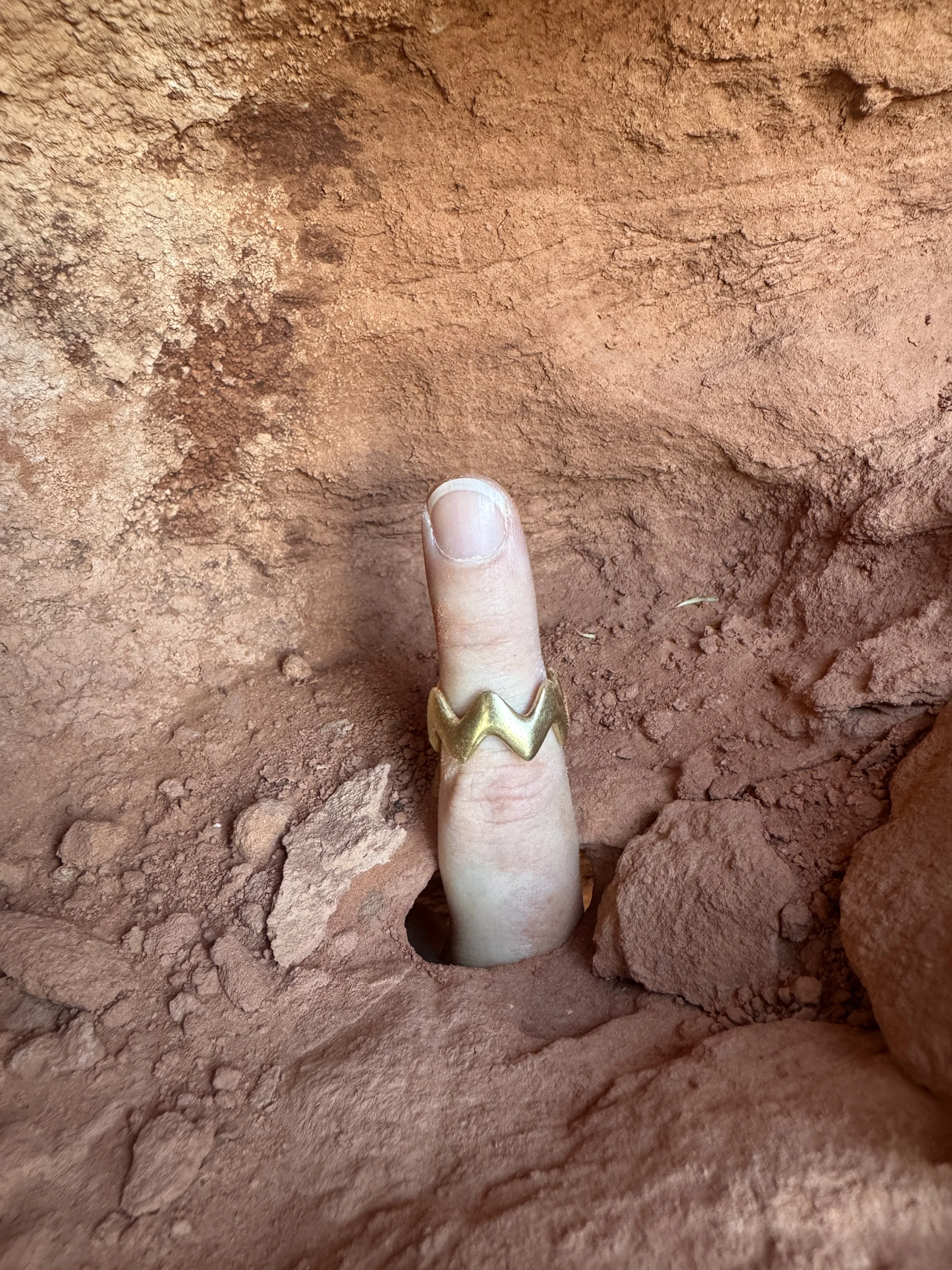 GemLost Desert ZigZag Ring in solid 18k gold worn on a finger emerging from a hole in red rock.
