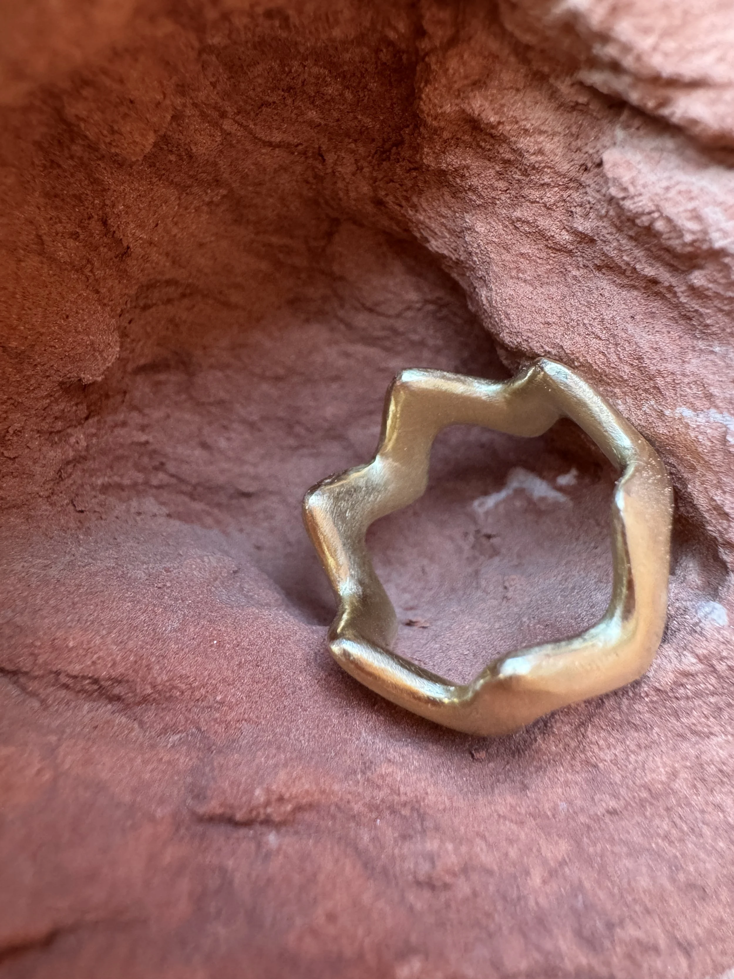 GemLost Desert ZigZag Ring in solid 18k gold shown from the inside, revealing its solid construction and continuous zigzag form, resting on red rock.