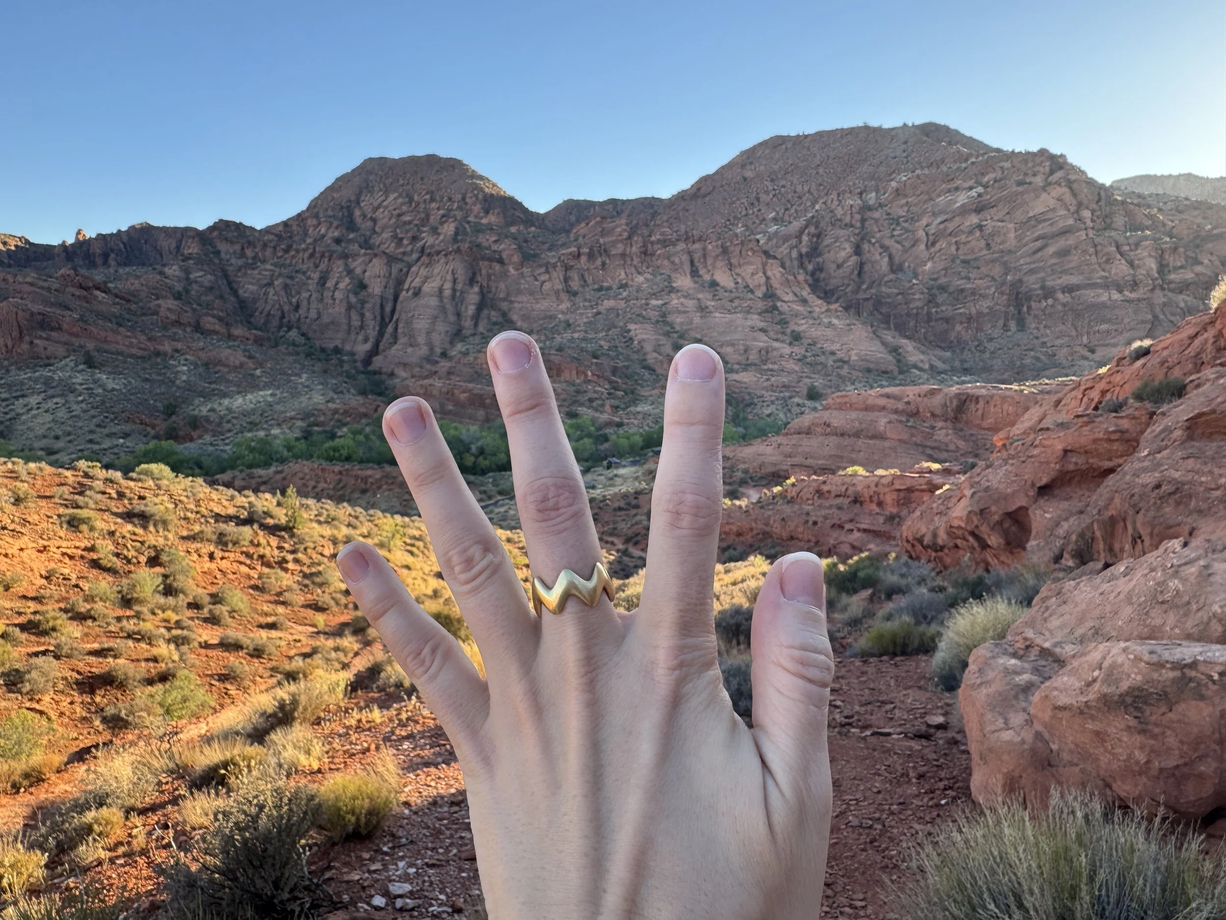GemLost Desert ZigZag Ring in solid 18k gold worn on a hand against a red rock desert mountain landscape.