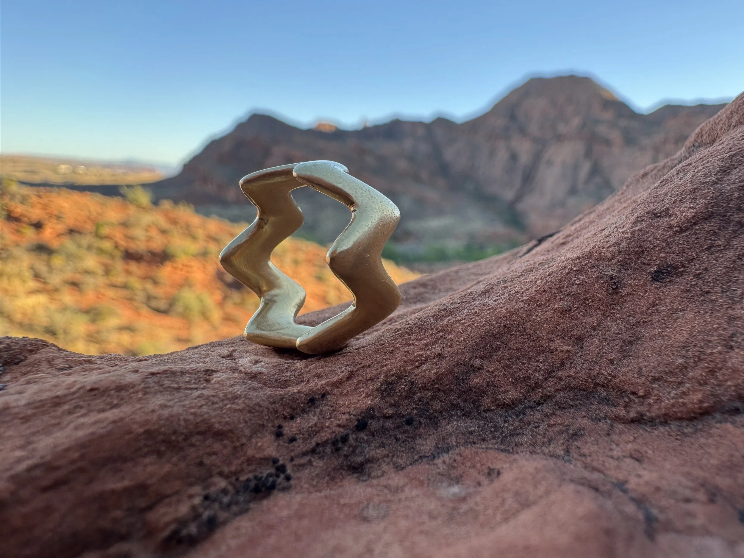 GemLost Desert Zigzag Ring in solid 18k gold resting on red sandstone with desert mountains in the background.