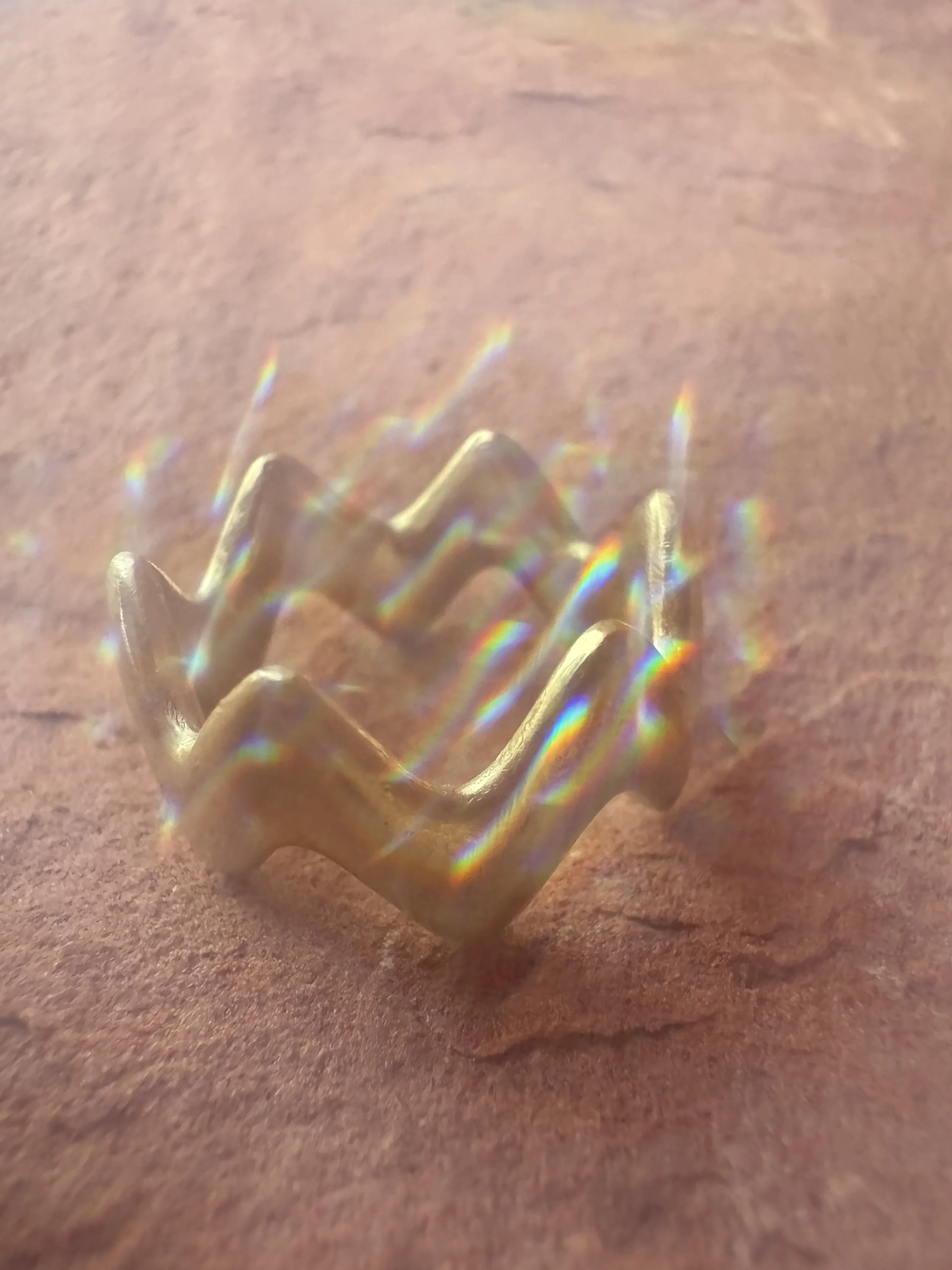 GemLost Desert ZigZag Ring in solid 18k gold resting on red rock with rainbow light refracting across the ring.