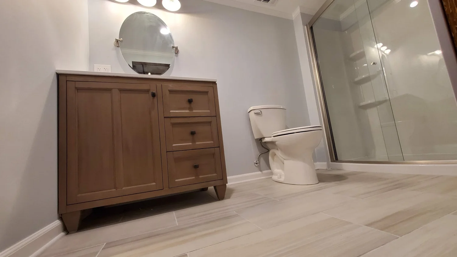 Finished basement bathroom in Rockaway NJ with wood vanity, tile floor and glass shower