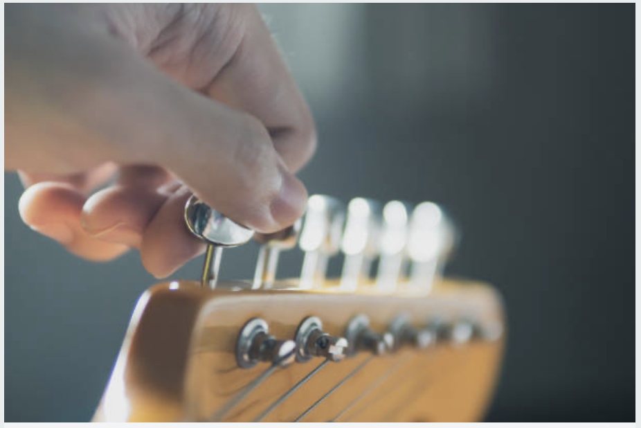 Close-up of a hand adjusting tuning pegs on a wooden guitar headstock.