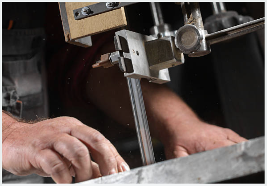 A person working with a metal cutting machine, possibly a bandsaw, using their hands to guide the material being cut.