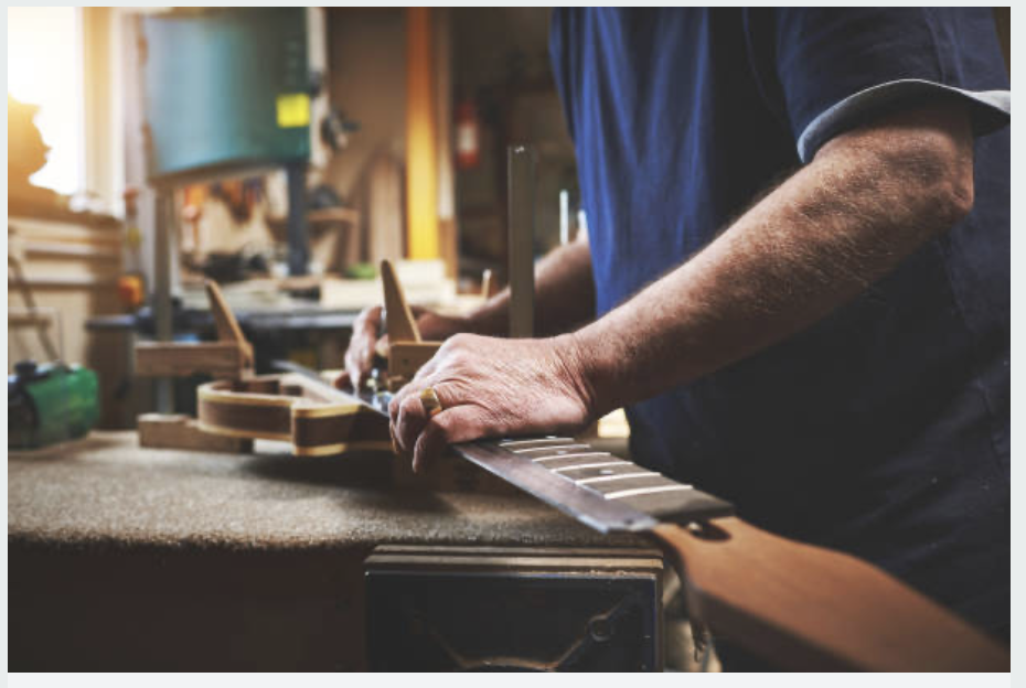 Close-up of a person working on building a guitar in a woodworking workshop.