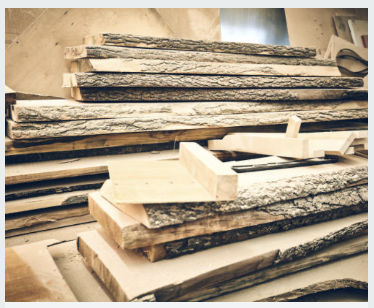 Stacks of rough cut wood planks and some smooth cut lumber in a woodworking shop.