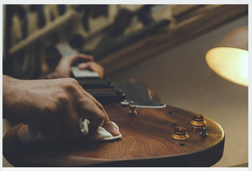 Person cleaning a wooden electric guitar with a cloth in a dimly lit room.
