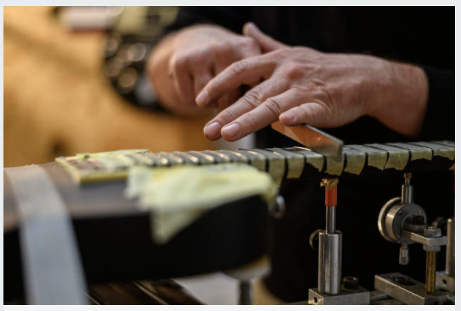 A person playing a metallophone, hitting metal bars with a mallet in a musical instrument workshop.