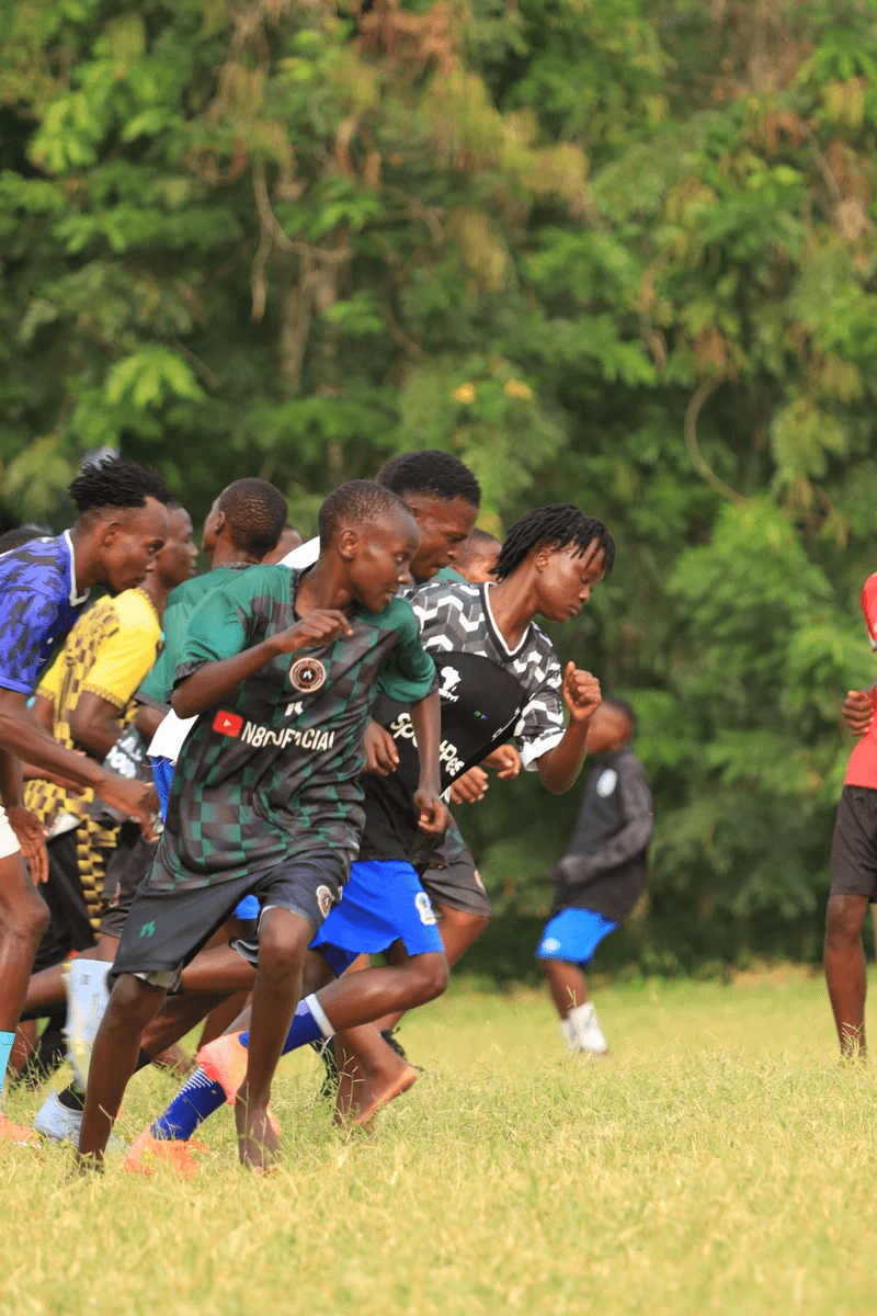 Young boys running on a grassy field, likely participating in a race or sporting event, with trees in the background.
