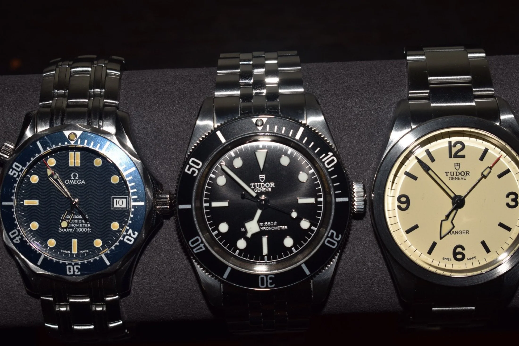 Three wristwatches with metal bands placed side by side on a black surface.