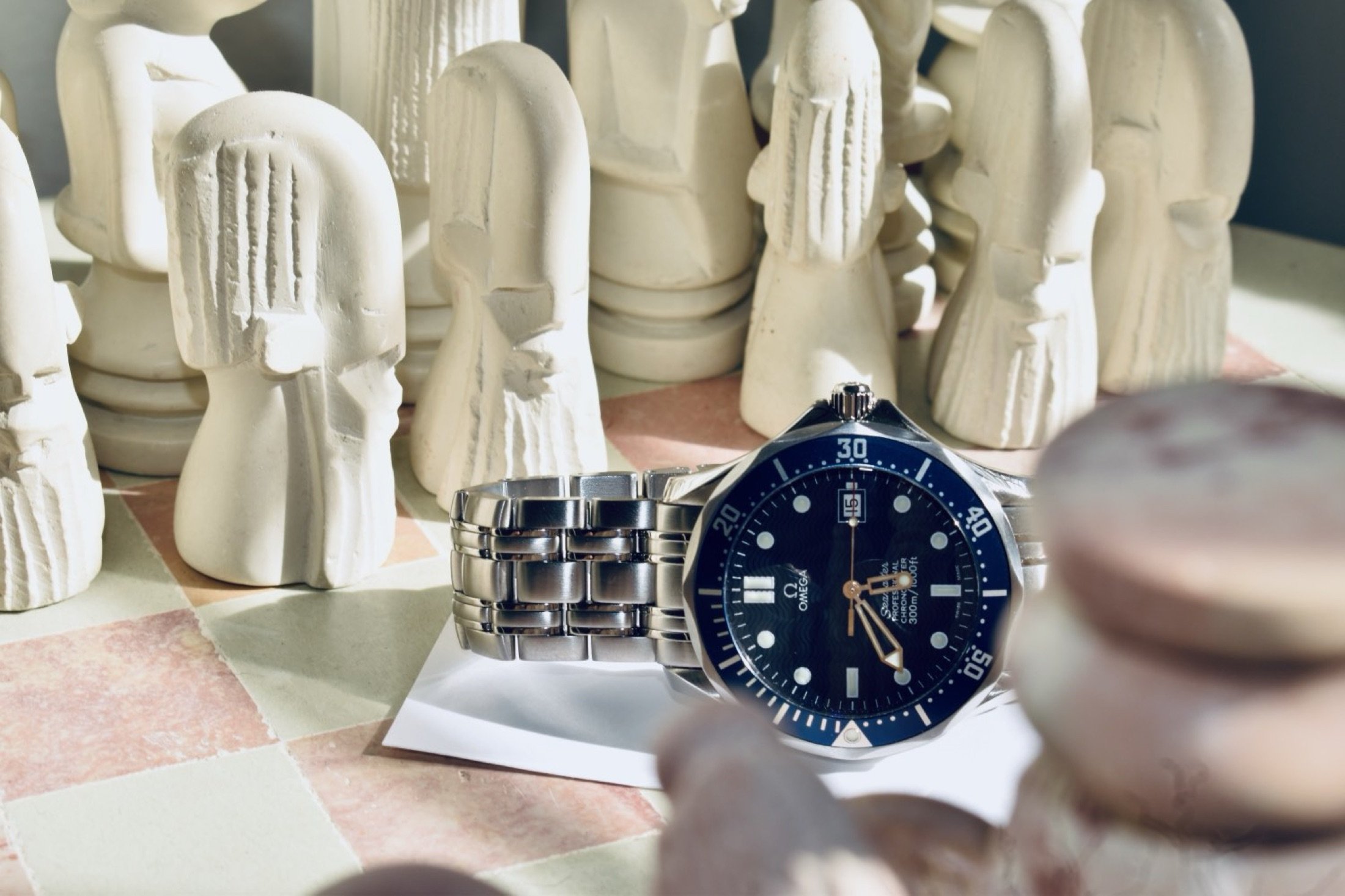 A collection of white decorative sculptures resembling abstract human faces and figures, with a silver Omega wristwatch placed among them on a surface.
