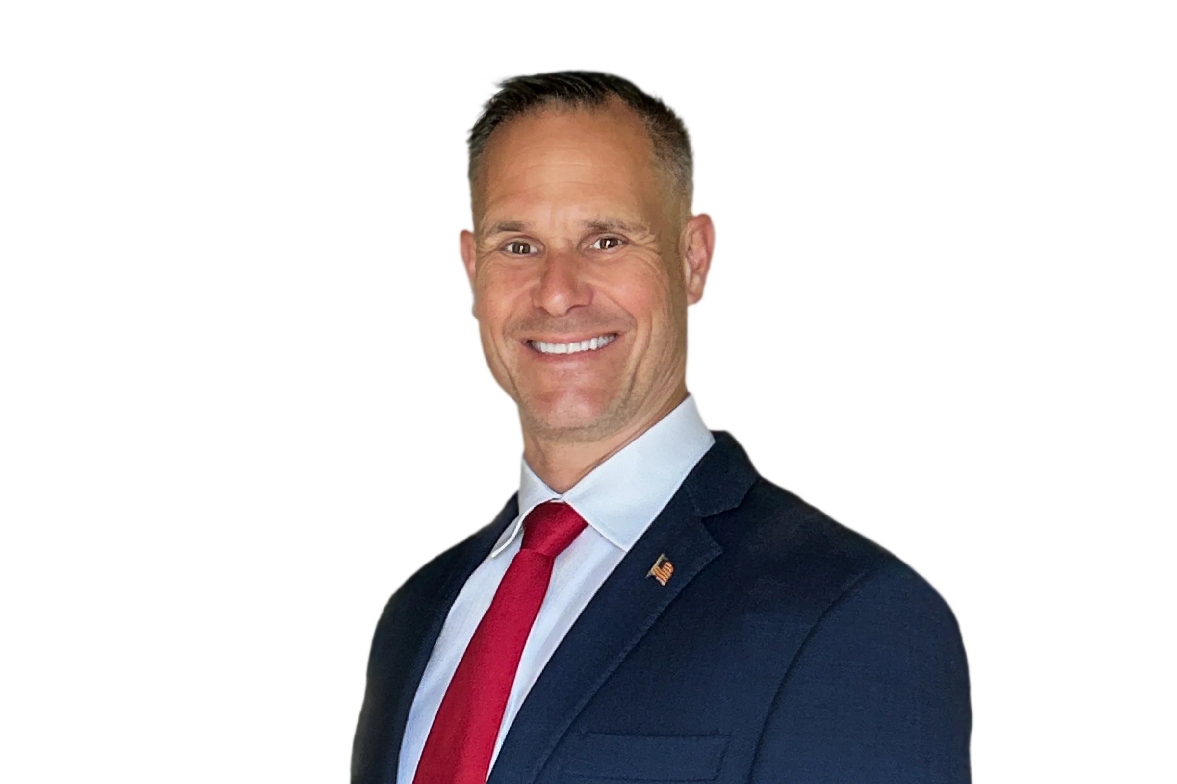 A smiling man in a dark suit, white shirt, and red tie, with an American flag lapel pin, against a white background.
