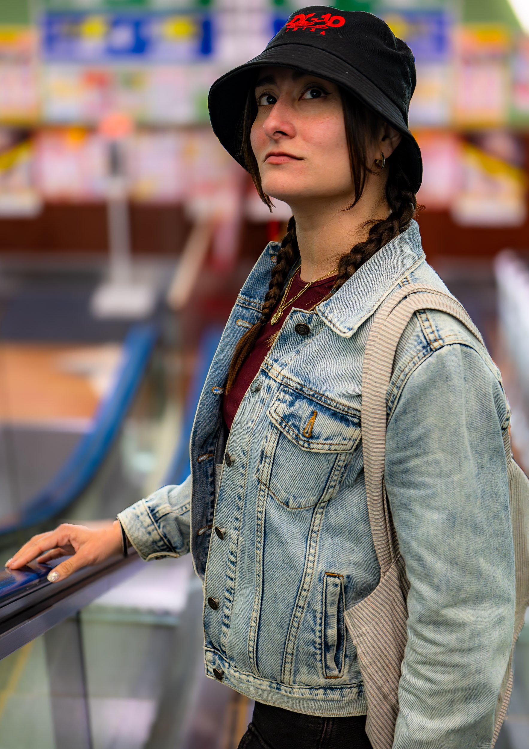 A woman with braided hair wearing a black bucket hat and denim jacket at a store checkout counter.
