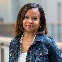 Woman with shoulder-length brown hair wearing a denim jacket and pearl necklace