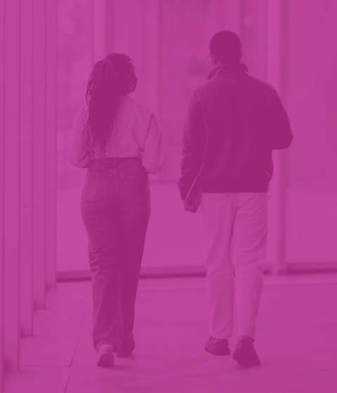 A man and a woman walking together in an indoor corridor, engaged in conversation, with the woman wearing a face mask.