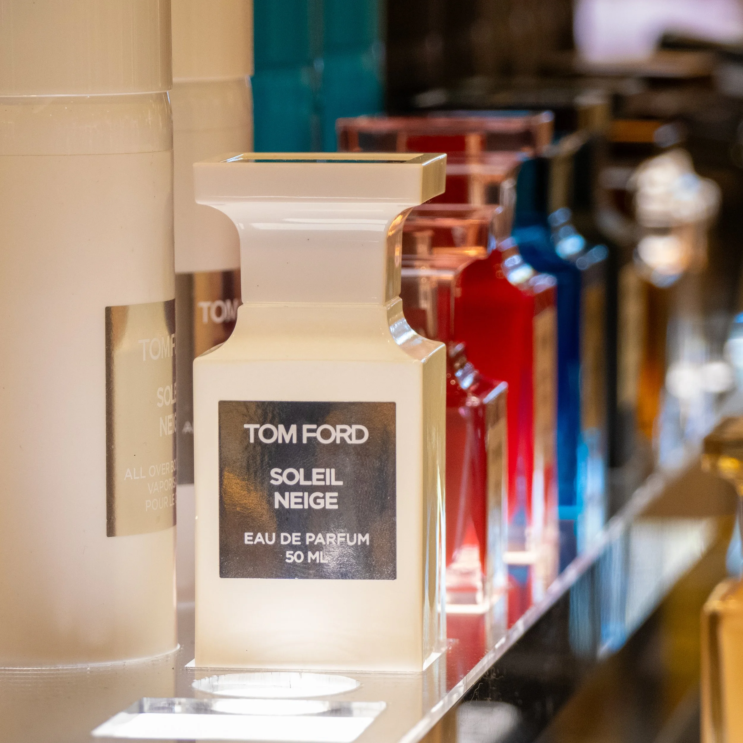 Close-up of perfume bottles on a store shelf, including Tom Ford Soleil Neige Eau de Parfum 50 ml.