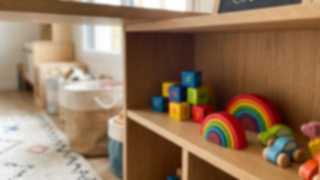 Étagère en bois avec des jouets en forme d'arc-en-ciel, cubes colorés et véhicules en bois, dans une salle de jeux pour enfants.