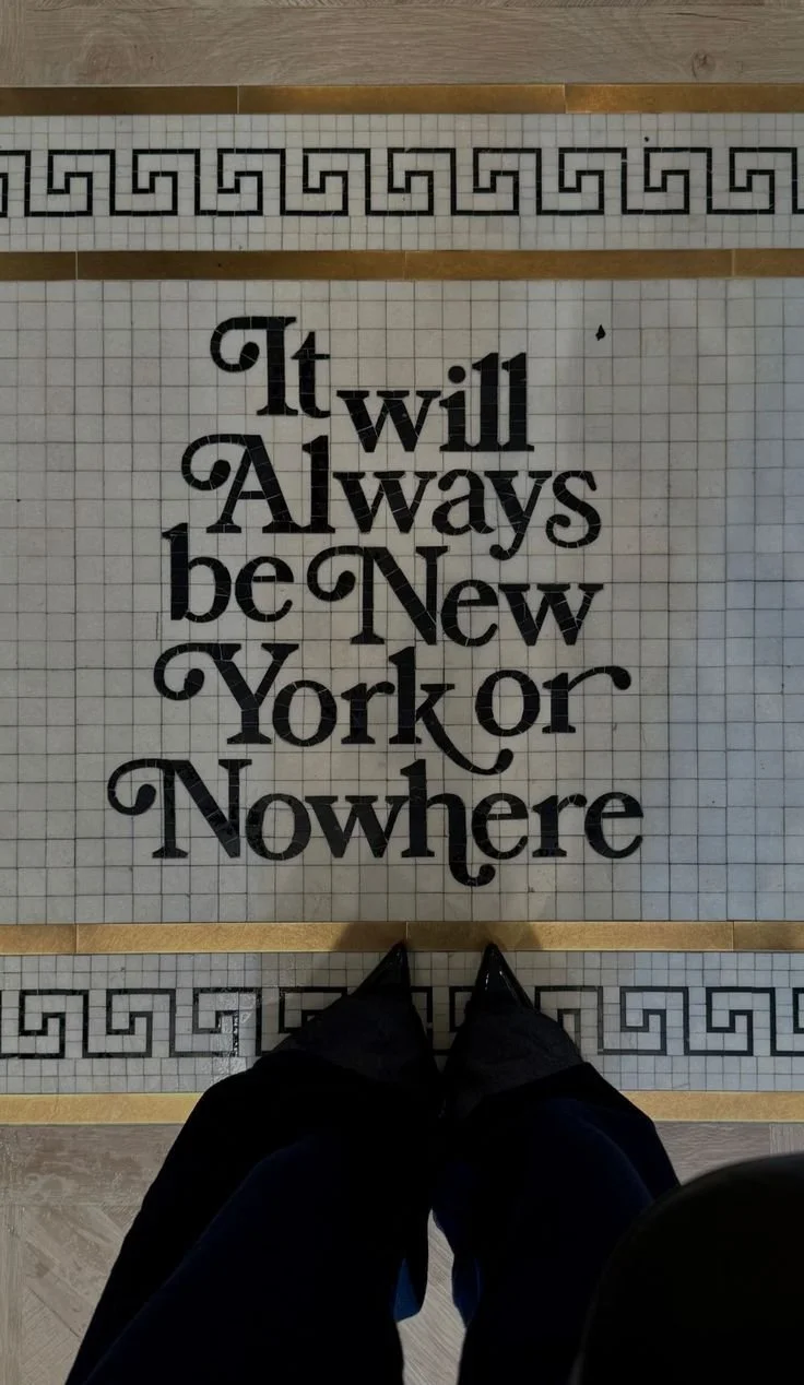 A tiled floor with black text that reads 'It will always be New York or Nowhere,' surrounded by decorative black and gold borders, and a person in dark clothing standing at the bottom of the image.