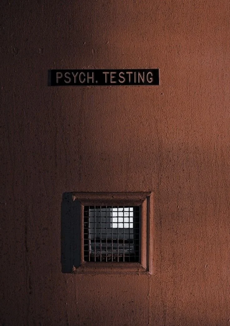 A wall with a sign reading 'PSYCH. TESTING' and a small vent with a metal grate below it.