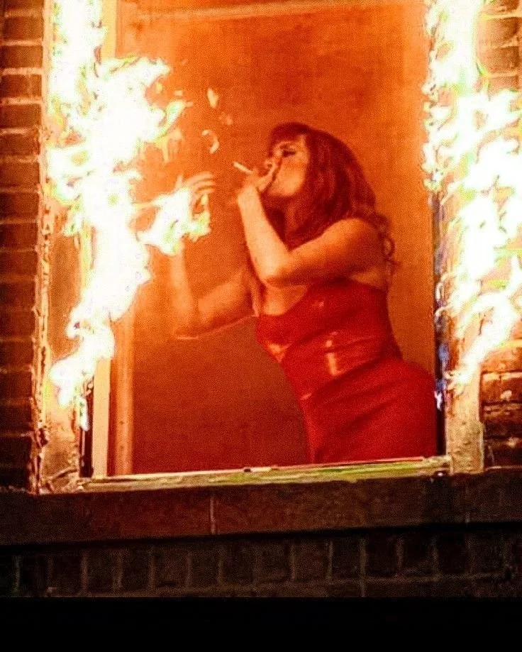 Woman in a red dress is breathing fire between two flames.