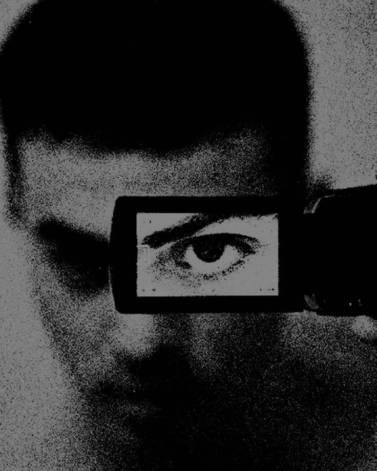 A person's face with a camera covering one eye, which displays a close-up of the person's eye.